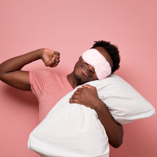 Person stretching with a sleep mask on and clutching a pillow.